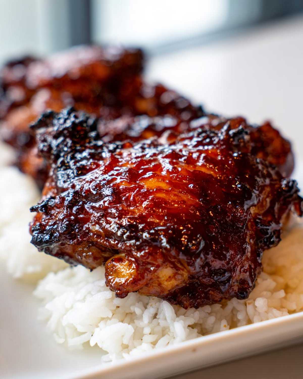 Close-up of a glazed, caramelized Sticky Sweet Chili Chicken Thighs resting on a bed of white rice.