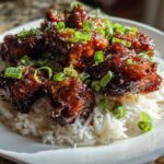 Close-up of Sticky Teriyaki Chicken Bites glazed in sauce, served over a bed of white rice and garnished with green onions.