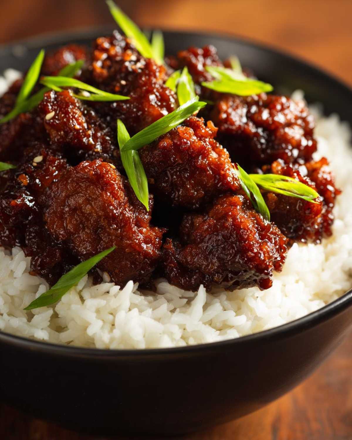 Close-up of glazed Sticky Teriyaki Chicken Bites piled high on a bed of fluffy white rice and garnished with green onions.