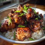 Close-up of glistening Sticky Teriyaki Chicken Bites piled high over fluffy white rice and garnished with sliced green onions.