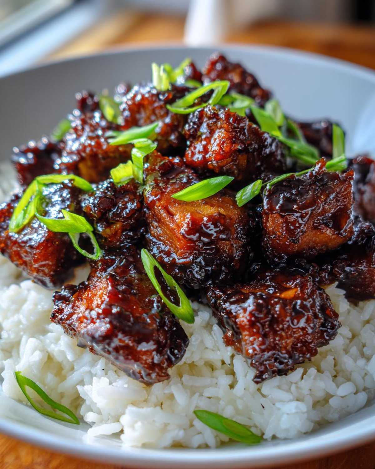 Close-up of Sticky Teriyaki Chicken Bites coated in a dark, glossy sauce, served over fluffy white rice and garnished with green onions.
