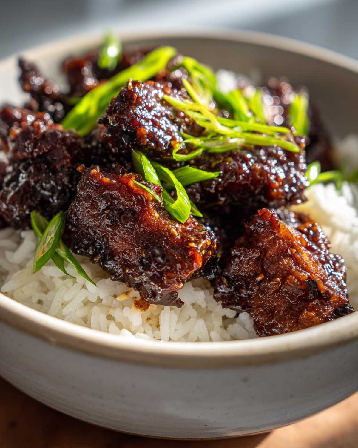 Close-up of glossy Sticky Teriyaki Chicken Bites piled high over fluffy white rice and garnished with fresh green onions.