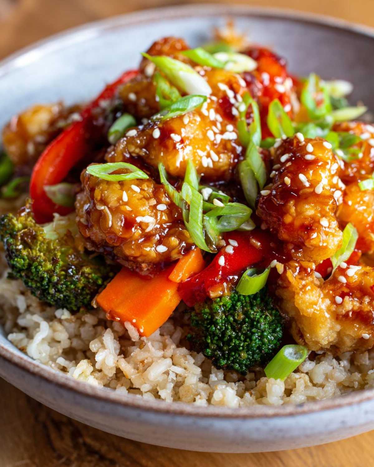 Close-up of a Sweet Chili Chicken Bowl featuring glazed chicken, broccoli, carrots, and brown rice, topped with sesame seeds.