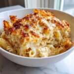 A close-up of a serving of Cheesy Chicken Alfredo Bake with Mozzarella in a white bowl, featuring a golden-brown, bubbly cheese crust.
