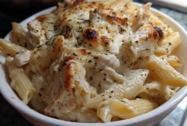 A close-up of a serving of Cheesy Chicken Alfredo Bake with Mozzarella, featuring penne pasta, chicken pieces, and a bubbly, browned cheese topping.
