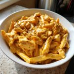 Close-up of a white bowl filled with rich, creamy Cheesy Chicken Queso Pasta, topped with cracked black pepper.