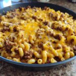 A close-up of Cheesy Ground Beef Pasta Skillet Comfort Food topped with melted cheddar cheese in a black skillet.