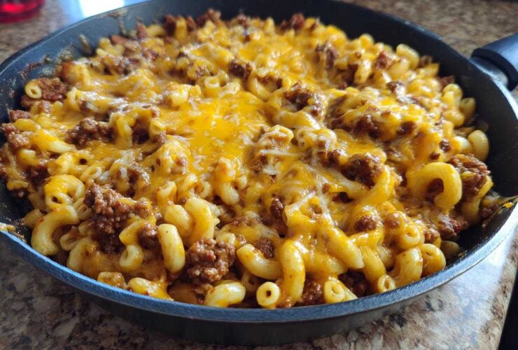 A close-up of Cheesy Ground Beef Pasta Skillet Comfort Food topped with melted cheddar cheese in a black skillet.