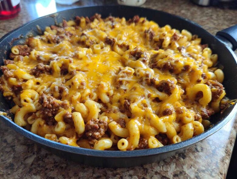 A close-up of Cheesy Ground Beef Pasta Skillet Comfort Food topped with melted cheddar cheese in a black skillet.