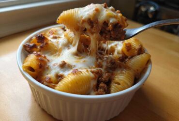 A fork lifts a spoonful of Cheesy Pasta Shells with Creamy Beef Sauce, showing long, gooey cheese pulls.