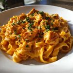 A close-up shot of rich, orange-hued Creamy Cajun Chicken Pasta featuring fettuccine noodles and seasoned chicken chunks, garnished with parsley.