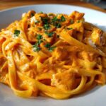 A close-up of a generous serving of Creamy Cajun Chicken Pasta featuring fettuccine noodles coated in a rich, orange-hued sauce with chunks of chicken, garnished with parsley.