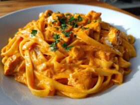 A close-up of a generous serving of Creamy Cajun Chicken Pasta featuring fettuccine noodles coated in a rich, orange-hued sauce with chunks of chicken, garnished with parsley.
