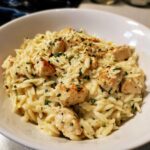 A close-up of Creamy Garlic Parmesan Orzo with Chicken served in a white bowl, garnished with parsley.