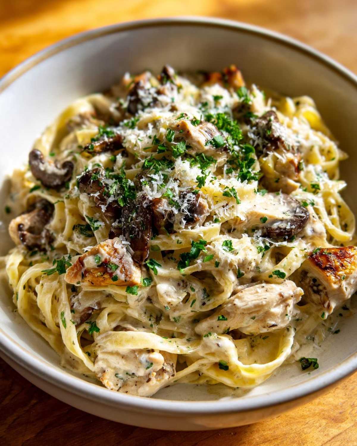 A close-up, appetizing bowl of Creamy Mushroom Chicken Pasta with Parmesan, topped with fresh parsley.