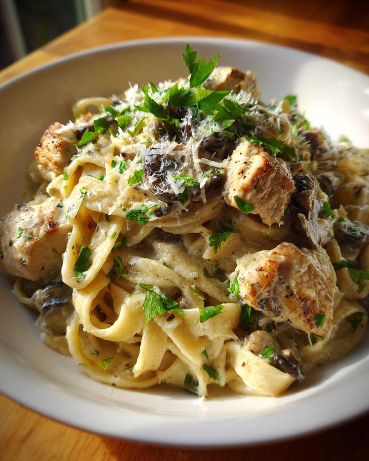 A close-up of a bowl of rich Creamy Mushroom Chicken Pasta with Parmesan, topped with fresh parsley.
