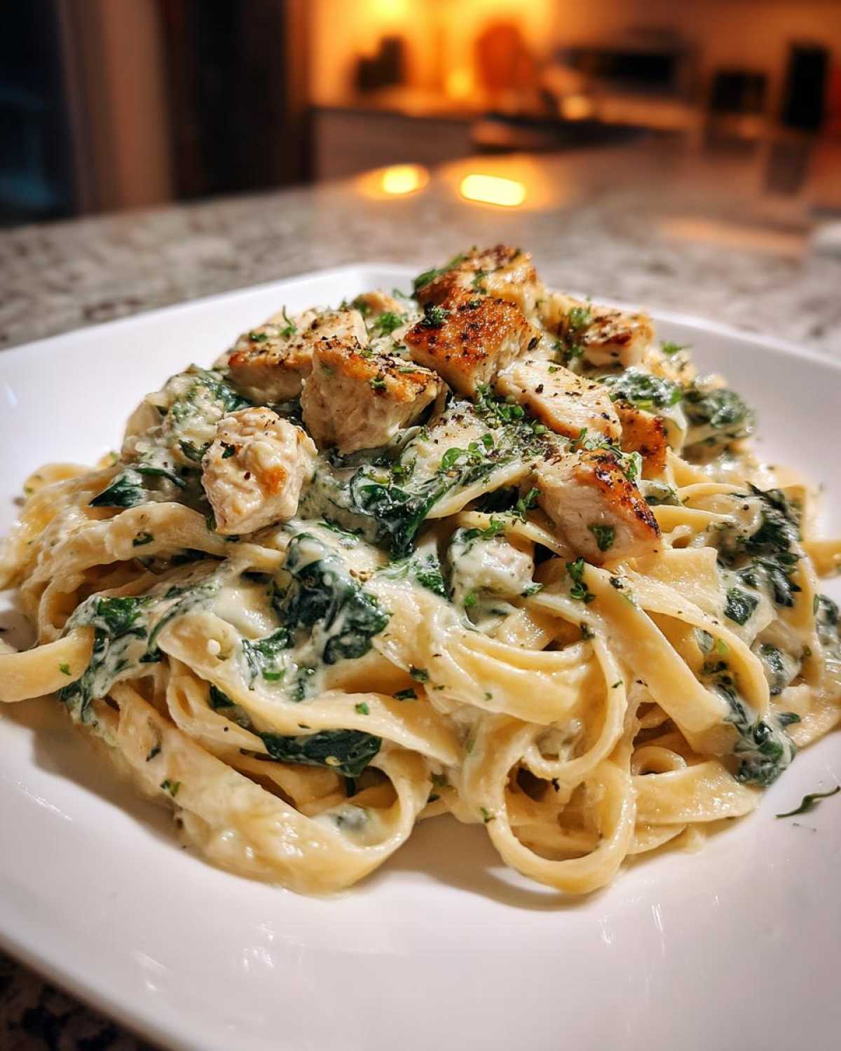 A close-up of Creamy Spinach Alfredo Pasta with Chicken served on a white plate, topped with seared chicken pieces.