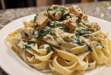 A close-up of rich Creamy Spinach Alfredo Pasta with Chicken served over fettuccine noodles on a white plate.