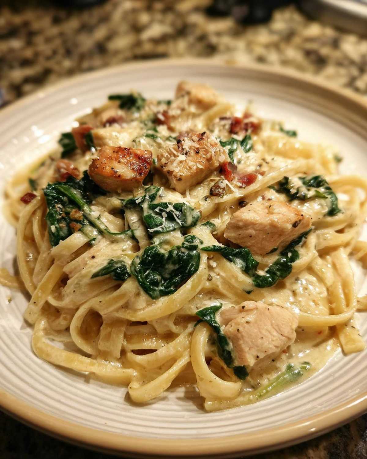 A close-up of Creamy Spinach Chicken Pasta with Garlic featuring fettuccine, chunks of chicken, wilted spinach, and grated Parmesan.