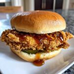 A close-up of a delicious Crispy Chicken Sandwich with Honey Sauce dripping over the fried chicken and pickles.