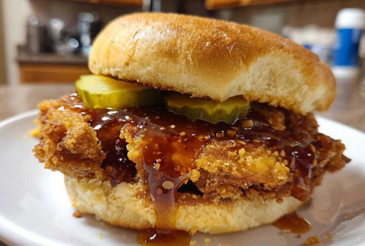 A close-up of a Crispy Chicken Sandwich with Honey Sauce, featuring a thick fried patty, pickles, and dripping glaze on a bun.