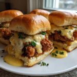 Four Crispy Chicken Sliders with Garlic Sauce piled high on a white plate, drizzled with creamy yellow sauce and parsley.