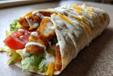 A delicious Crispy Chicken Wrap stuffed with fried chicken pieces, lettuce, tomato, cheese, and drizzled with creamy garlic sauce.