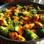 Close-up of vibrant Garlic Butter Chicken and Broccoli Stir Fry glistening in a dark skillet.