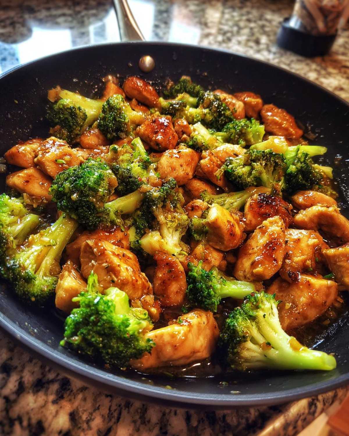 Close-up of Garlic Butter Chicken and Broccoli Stir Fry sizzling in a dark skillet.