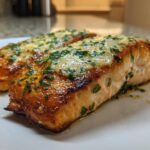 Two perfectly cooked fillets of Garlic Butter Salmon with crispy edges, topped with melted butter sauce and fresh parsley.