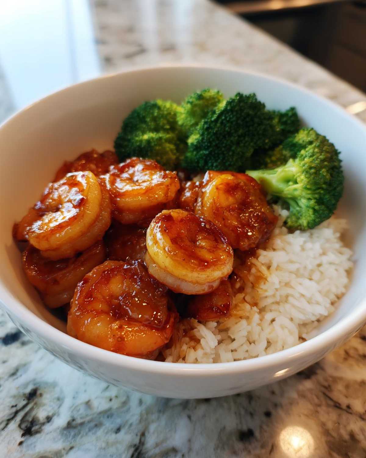 Close-up of a white bowl containing Honey Garlic Shrimp Bowl Quick Dinner with white rice and steamed broccoli florets.