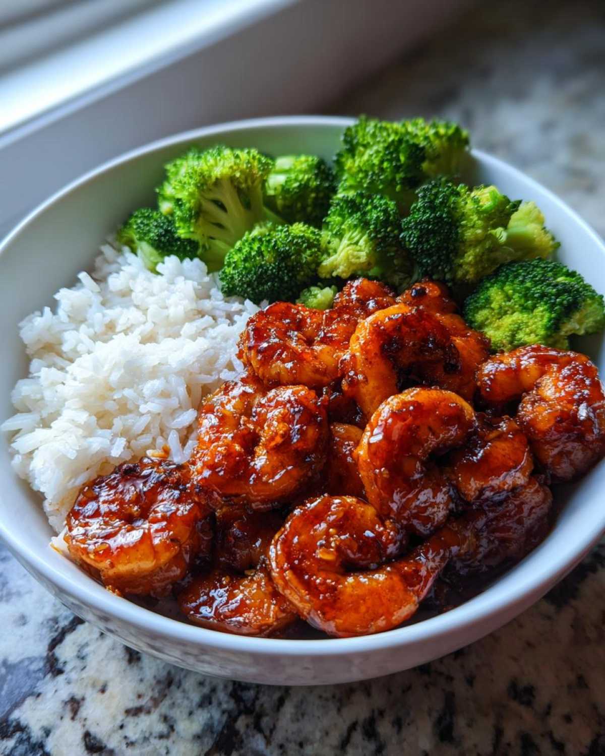 A white bowl filled with Honey Garlic Shrimp Bowl Quick Dinner ingredients: white rice, steamed broccoli, and glossy, glazed shrimp.