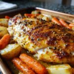 Close-up of a juicy Honey Mustard Chicken Bake with roasted carrots and potatoes on a sheet pan.
