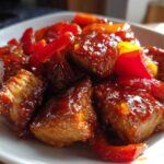 Close-up of glossy Honey Sriracha Chicken Skillet pieces coated in sweet and spicy sauce with red bell peppers.