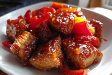 Close-up of glossy Honey Sriracha Chicken Skillet pieces coated in sweet and spicy sauce with red bell peppers.