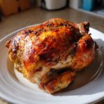A whole, perfectly cooked Lemon Herb Roasted Chicken with golden brown, crispy skin covered in herbs, resting on a white plate.