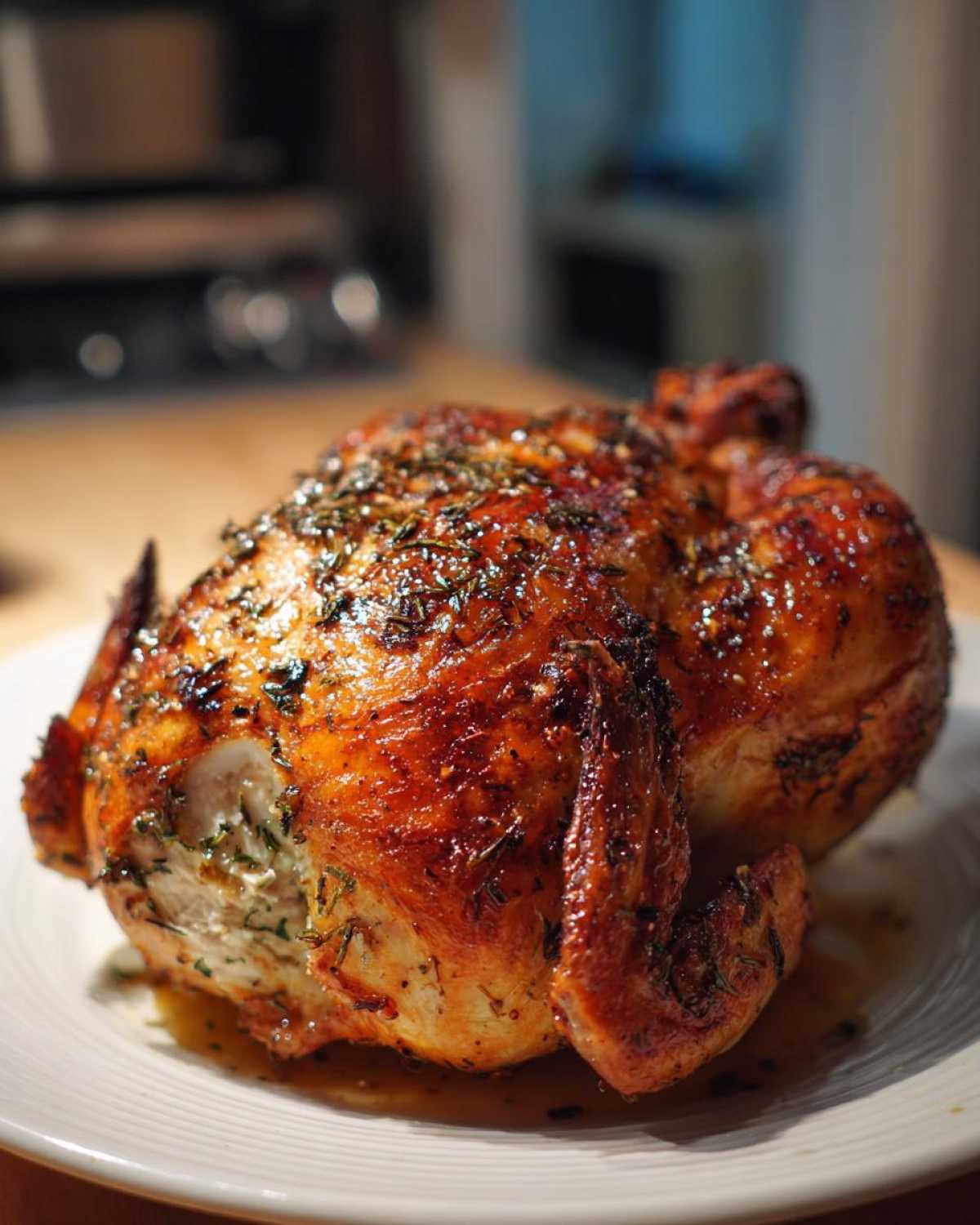 A whole, perfectly roasted Lemon Herb Roasted Chicken with glistening, crispy skin covered in herbs, resting on a white plate.