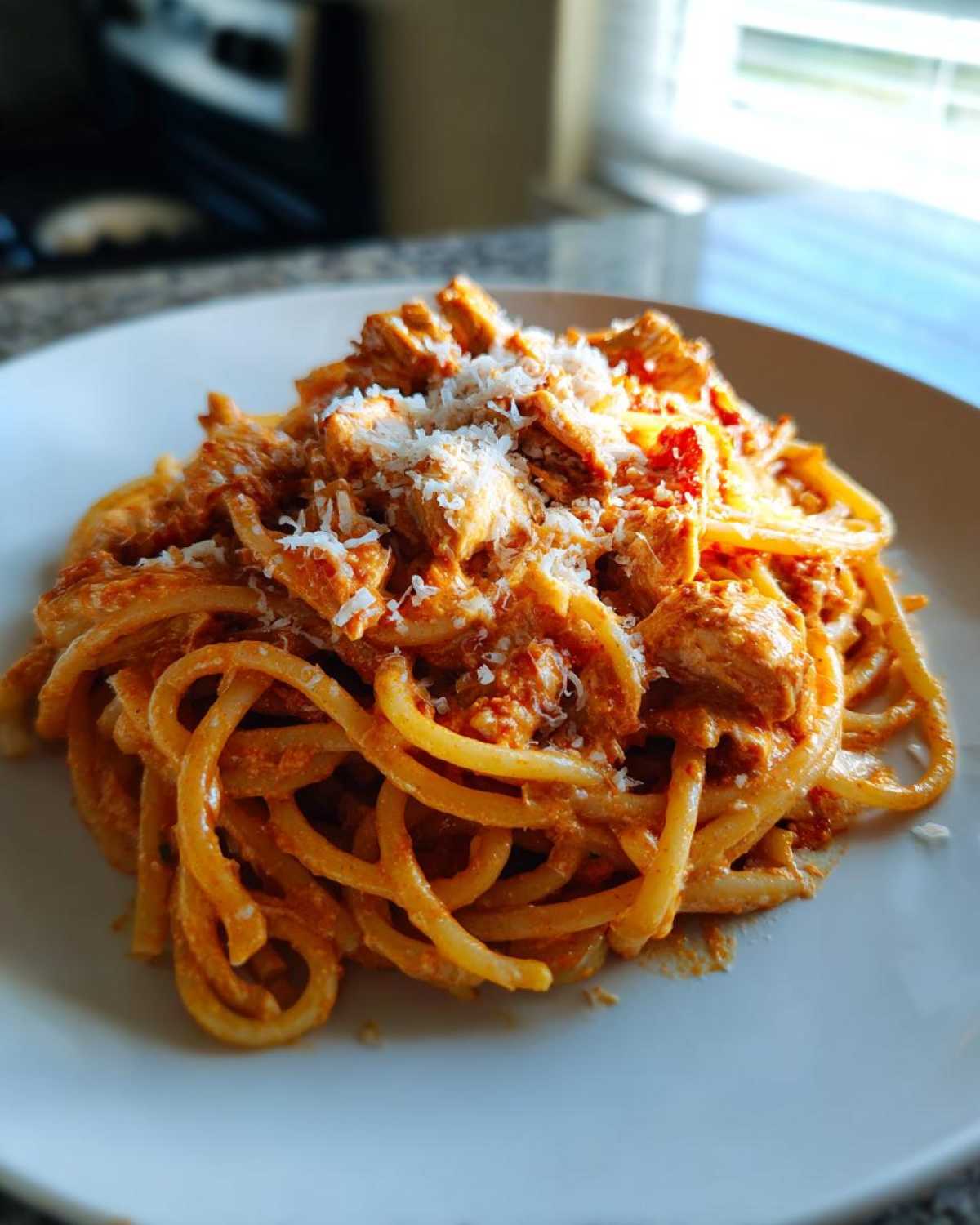 A close-up of a serving of One Pot Creamy Tomato Pasta with Chicken topped with grated Parmesan cheese on a white plate.