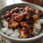 Close-up of a bowl filled with white rice topped generously with glazed, sticky BBQ chicken pieces.