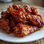 A close-up of several Sticky Sweet Chili Chicken Wings Oven Baked piled high on a white plate, glistening with sauce.