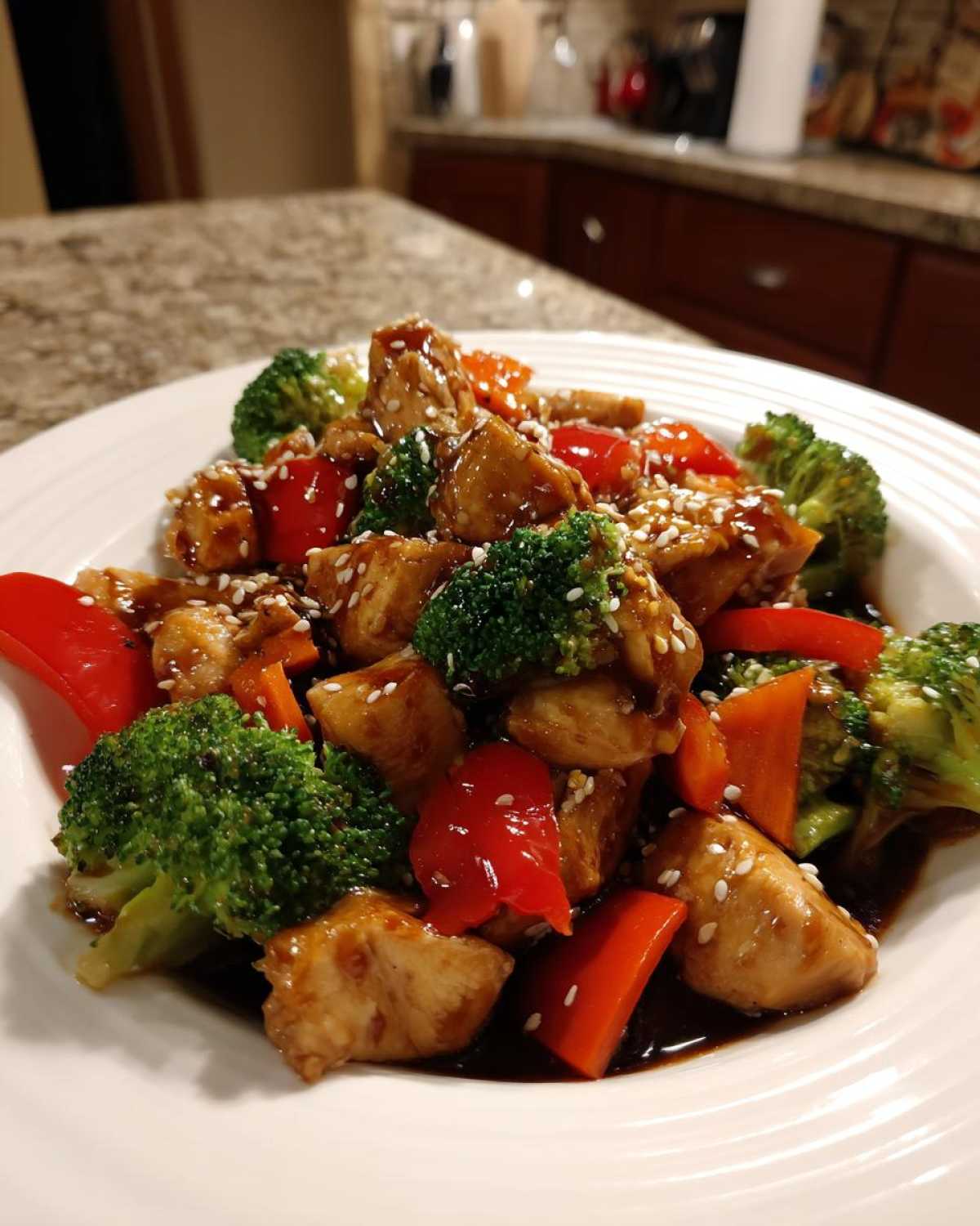 Close-up of a serving of Sticky Teriyaki Chicken Stir Fry Quick Meal with broccoli and red peppers, topped with sesame seeds.