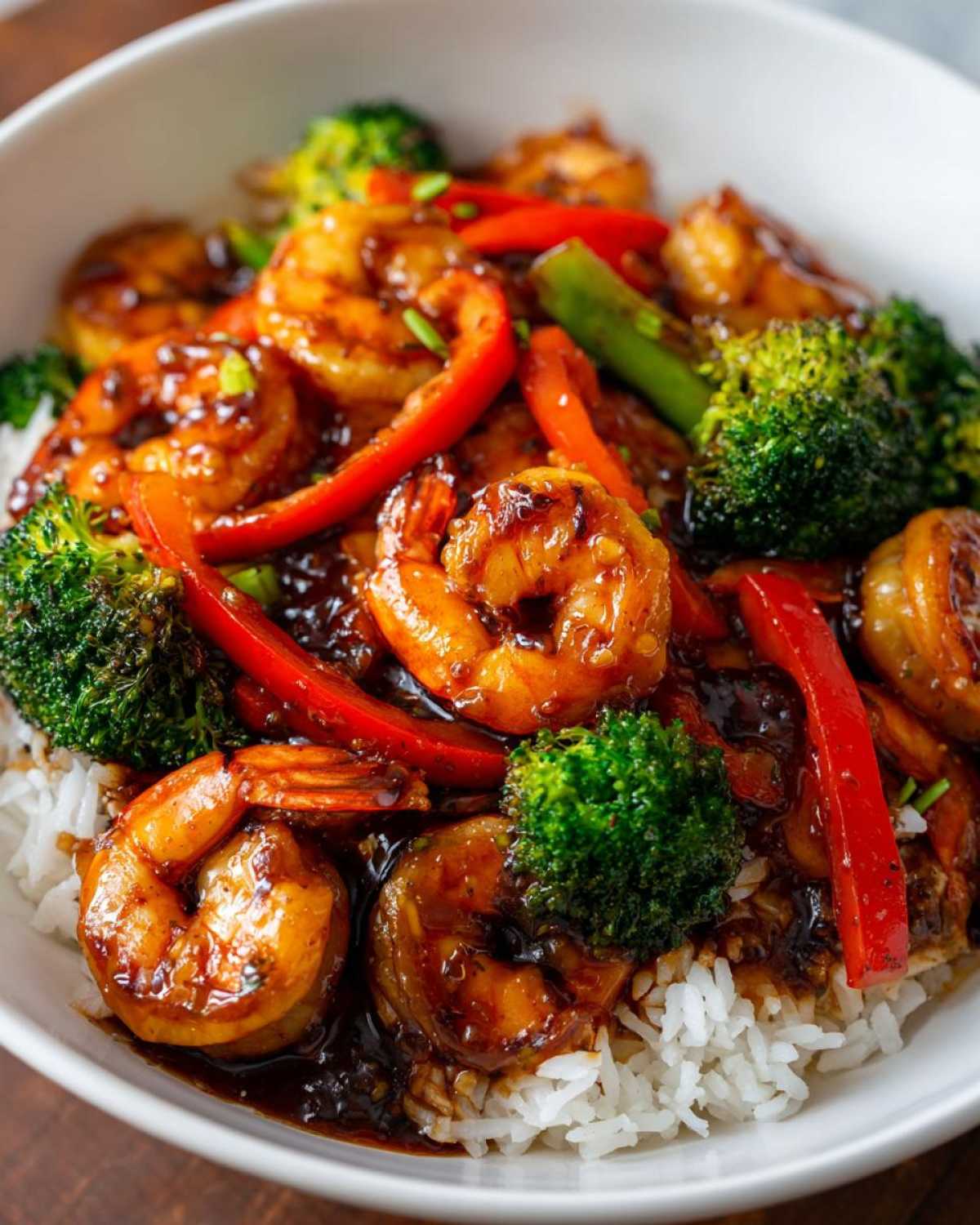 A close-up of a bowl containing Sticky Teriyaki Shrimp Stir Fry Meal served over white rice with broccoli and red peppers.